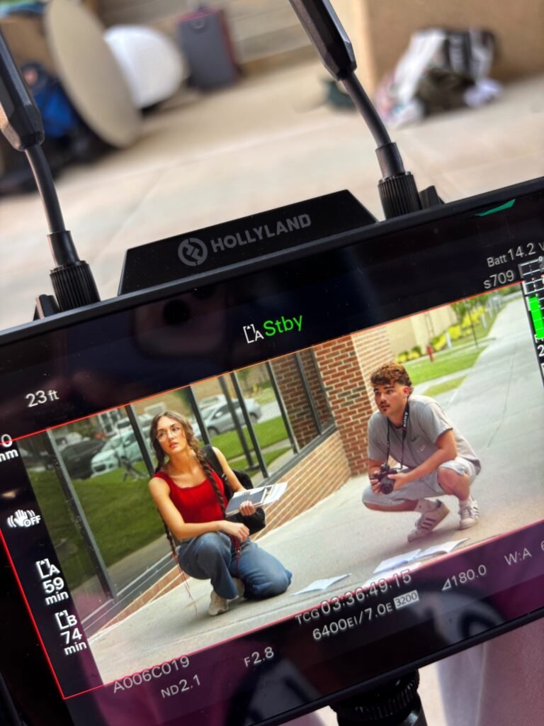 Production monitor showing two actors preparing a scene for Blue After Gold outside a brick building.